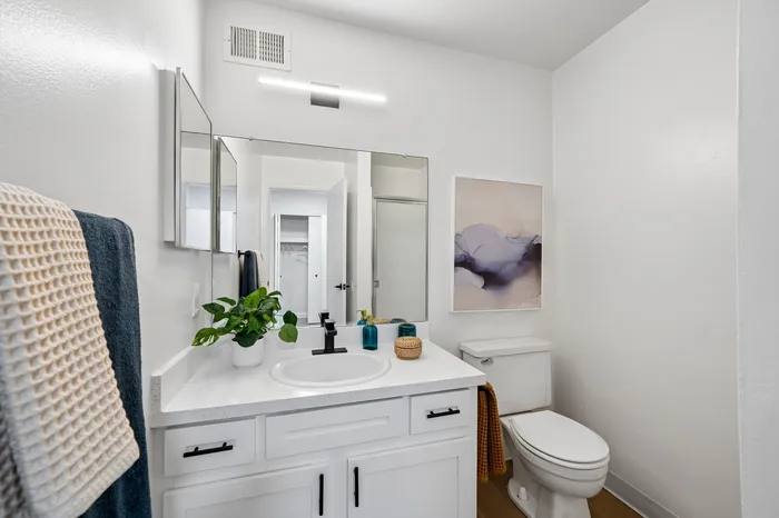 Bright and modern bathroom featuring a sleek white vanity, elegant wall art, and vibrant green plant for a touch of nature.