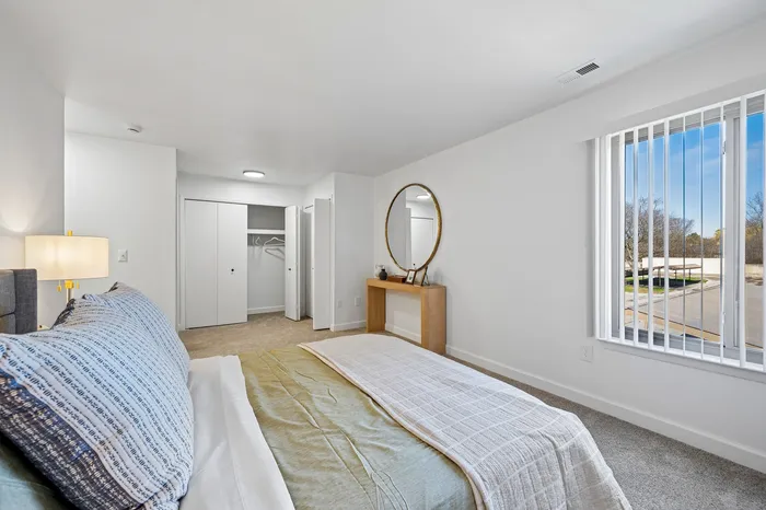 Bright and inviting bedroom with plush carpeting, large window for natural light, and sleek closet space providing ample storage.