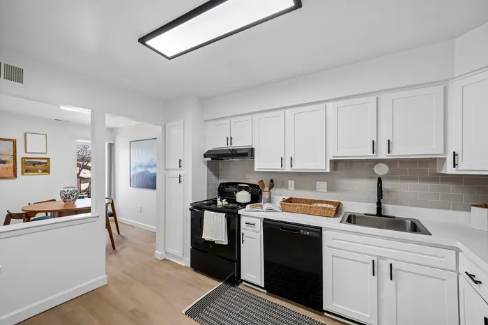 Modern kitchen featuring sleek white cabinets, elegant black appliances, and a cozy dining area with stylish decor.