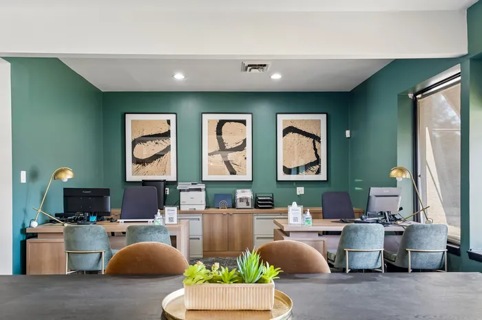 Modern office space featuring elegant green walls, stylish artwork, and sleek furniture with plush seating.