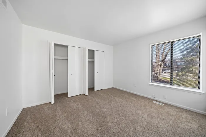 Bright and airy bedroom with a large window, plush carpet, and spacious double closets for ample storage.