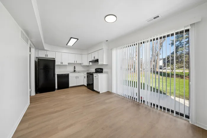 Bright and airy kitchen with sleek black appliances, modern white cabinetry, and large sliding doors opening to a lush green view.