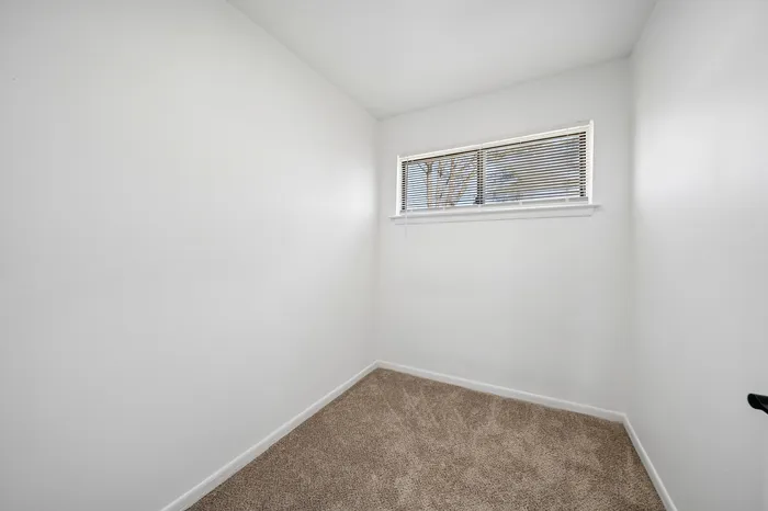 Cozy room with plush carpet and a window, perfect for a home office or creative space.
