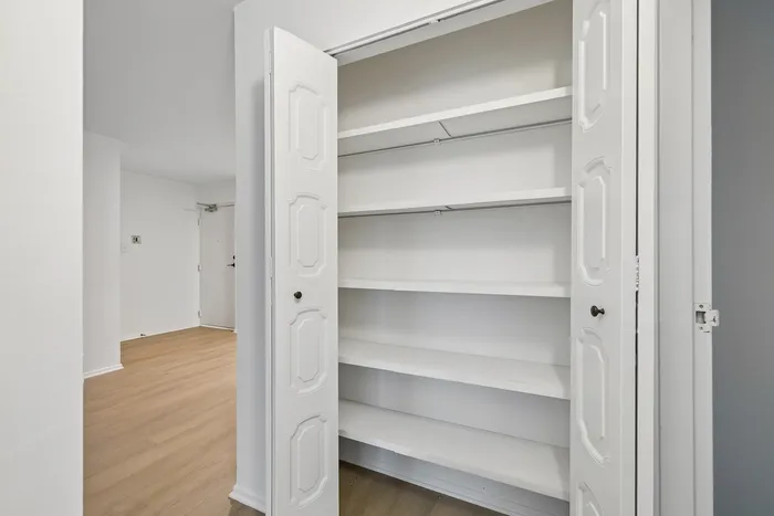 Bright apartment hallway with elegant built-in shelving, light wood flooring, and modern white doors.