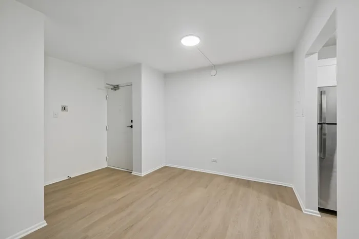 Bright, minimalist apartment entryway with modern wood flooring and sleek stainless steel kitchen appliances.