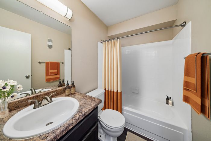 Modern bathroom featuring a sleek countertop, elegant sink, and a pristine bathtub with a stylish curtain, accented by warm hues and tasteful decor.