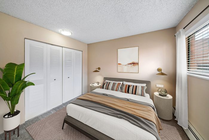 Elegant bedroom with modern decor, featuring a cozy bed, large closet, stylish artwork, and a vibrant plant next to a sunlit window.