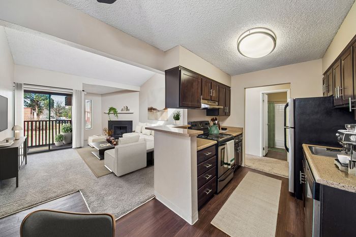 Chic open-plan layout featuring a cozy living room with fireplace, modern kitchen with dark wood cabinets, and sliding doors leading to a private balcony with lush views.