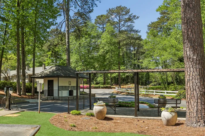 Charming outdoor space with seating area under a pergola, surrounded by lush greenery and blooming flowers, perfect for relaxation and enjoying nature.