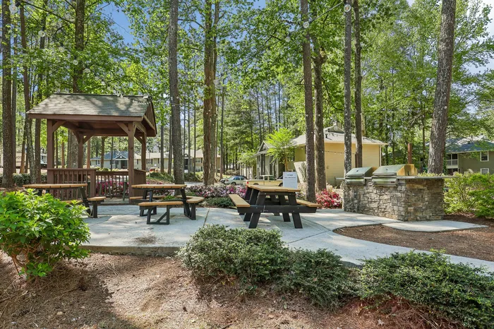 Charming outdoor picnic area with wooden tables, surrounded by lush greenery and string lights, perfect for relaxing gatherings.
