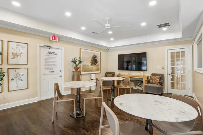 Chic resident lounge featuring modern decor, round marble tables, and a large TV for relaxation and social gatherings.
