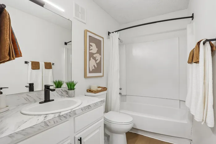 Bright and modern bathroom with sleek marble countertop, stylish black fixtures, and elegant wall decor.