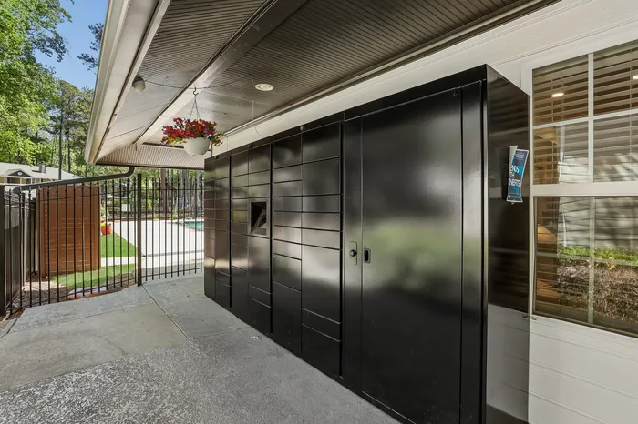 Modern outdoor parcel locker area near a gated pool, surrounded by lush greenery and featuring a hanging flower basket for a welcoming touch.