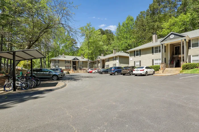 Charming apartment complex surrounded by lush greenery, featuring convenient parking and bicycle storage in a serene neighborhood setting.