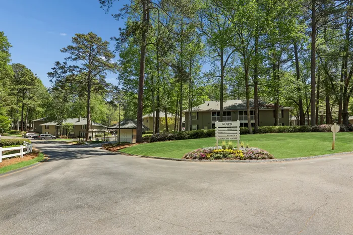 Inviting apartment community nestled among lush trees, featuring manicured lawns and vibrant flower beds under a clear blue sky.