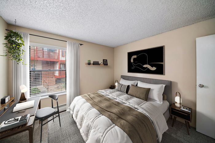 Cozy bedroom with a modern desk setup, plush bedding, elegant artwork, and a large window with ample natural light.