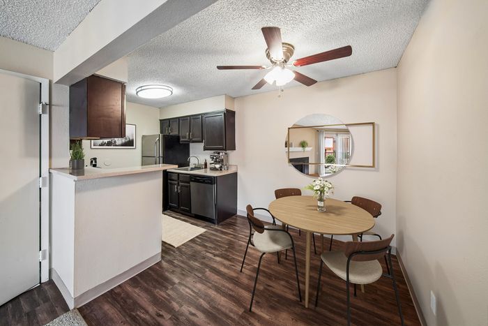 Charming apartment dining area with a modern kitchen, featuring sleek dark cabinetry, a ceiling fan, and stylish wood flooring. Perfect blend of comfort and contemporary design.