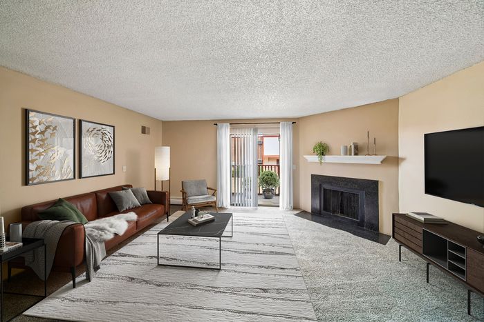 Inviting living room featuring modern decor, a cozy brown leather sofa, stylish art pieces, and a sleek fireplace, opening to a sunny balcony.