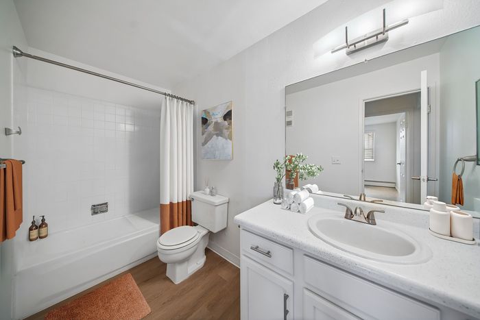Bright and modern bathroom featuring a sleek white vanity, stylish faucet, and relaxing bathtub with elegant curtains.