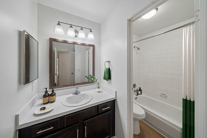 Elegant bathroom showcasing a modern vanity with a large mirror, soft lighting fixtures, and a pristine bathtub with a tiled wall.