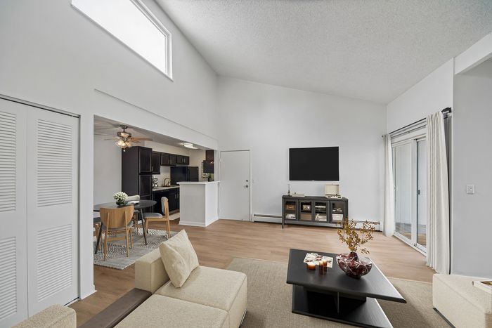 Modern living room with high ceilings, featuring an open layout to kitchen, elegant furnishings, and abundant natural light.