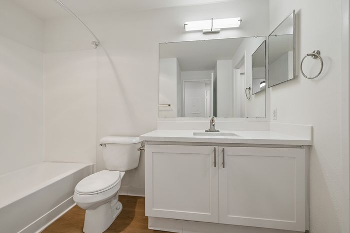 Bright and modern bathroom featuring sleek white cabinetry, elegant fixtures, and a spacious mirror, perfect for contemporary living.