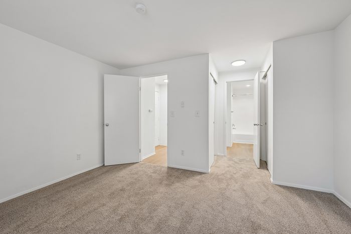 Bright and airy bedroom with plush carpeting and modern white doors leading to a pristine bathroom.