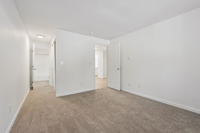 Bright, spacious bedroom with plush carpet and a view of the hallway leading to a modern bathroom.