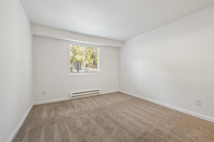 Bright, inviting bedroom with soft beige carpet and a large window offering natural light and scenic views.