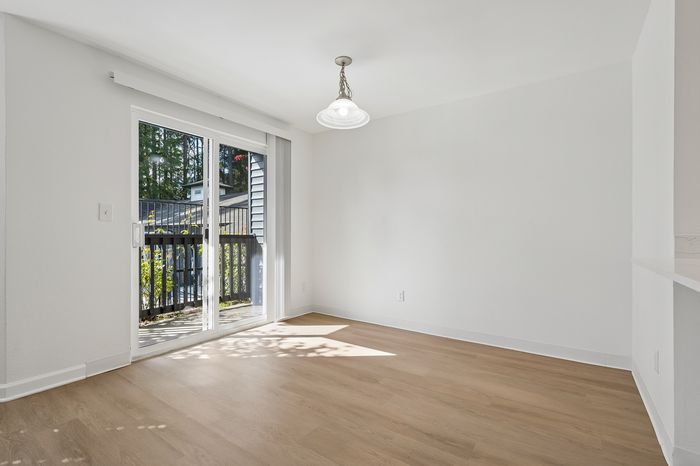 Bright and airy apartment space with sliding glass doors opening to a charming balcony, featuring elegant wood flooring and modern light fixture.