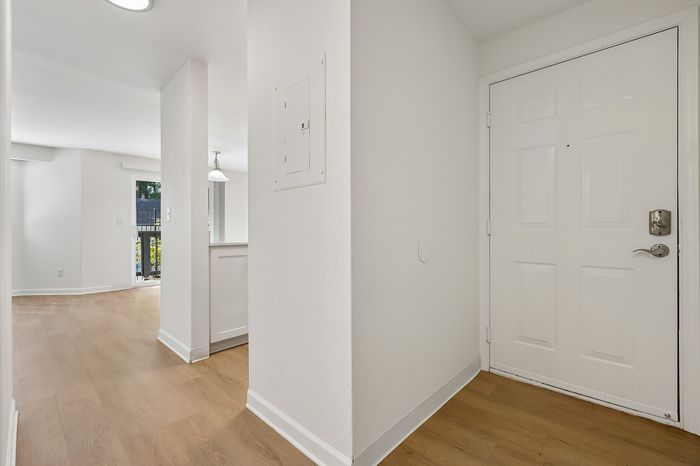 Inviting apartment entryway with sleek wooden flooring leading to a sunlit open area, perfect for a cozy and welcoming atmosphere.