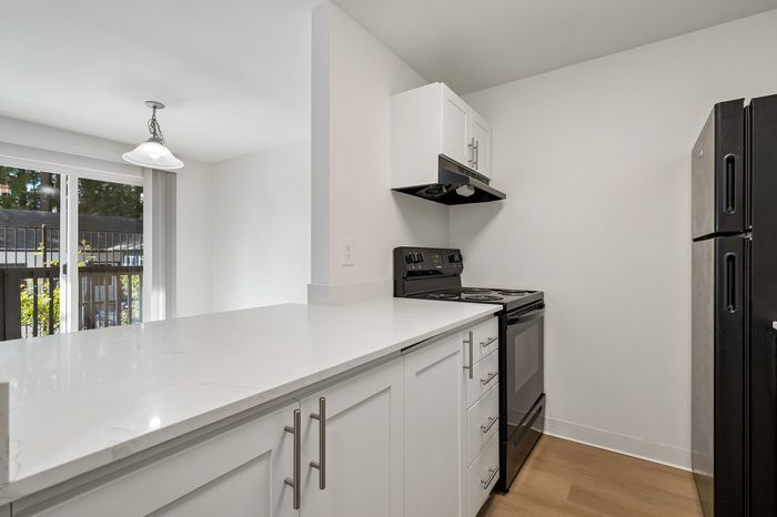 Modern kitchen with sleek white cabinetry and elegant black appliances, featuring a stylish countertop and abundant natural light.