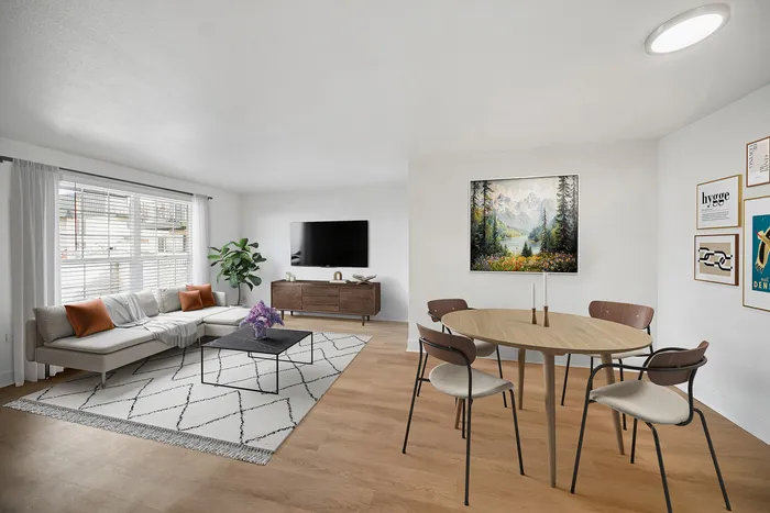 Bright and modern living-dining area with stylish decor, featuring a cozy sectional sofa, vibrant artwork, and elegant wooden furniture.