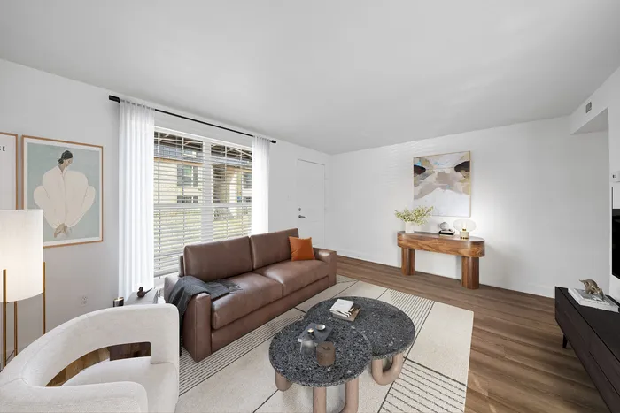 Bright and welcoming living room featuring modern decor, a comfortable leather sofa, and large windows with sheer curtains.