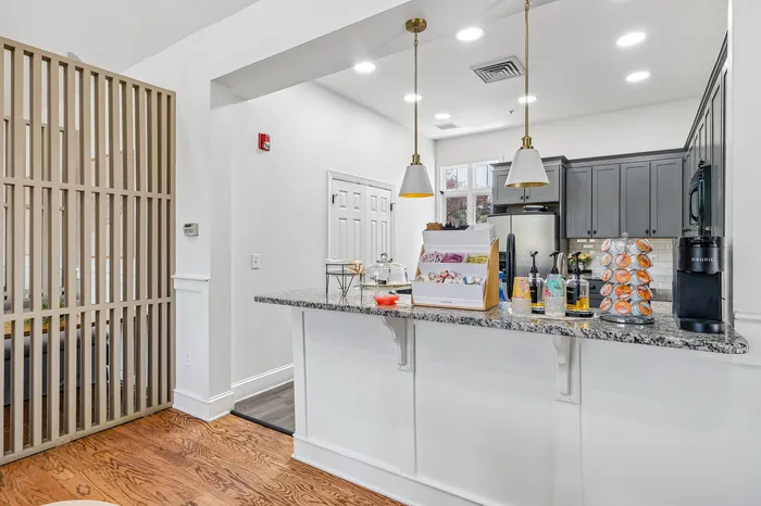 Modern kitchen with sleek granite countertops, stylish pendant lighting, and elegant cabinetry, featuring a cozy coffee station and bright, airy ambiance.
