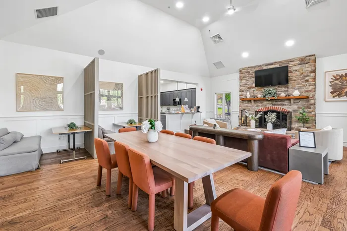 Inviting open-concept living area with a sleek dining table, vibrant orange chairs, and a cozy stone fireplace, perfect for gatherings.