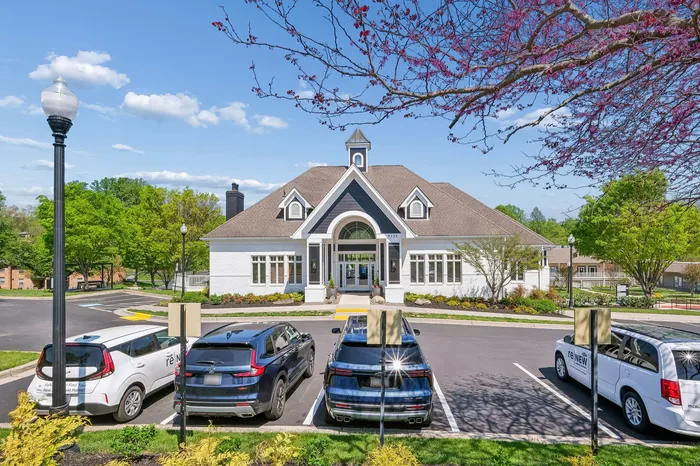 Charming residential building with elegant gabled roof, lush landscaping, and ample parking, showcasing vibrant spring foliage.
