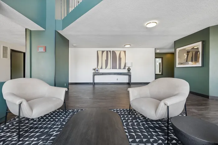 Sleek modern living area with plush beige chairs, geometric rug, and abstract wall art, offering a stylish and inviting ambiance.