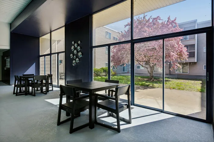 Contemporary indoor dining area with stylish dark tables and large glass windows showcasing a vibrant flowering tree outside.