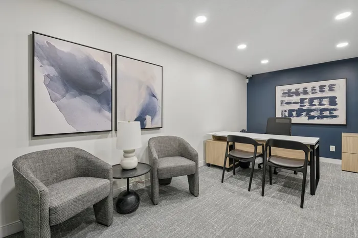 Chic office space featuring modern art, stylish grey armchairs, and a sleek desk against a sophisticated blue accent wall.