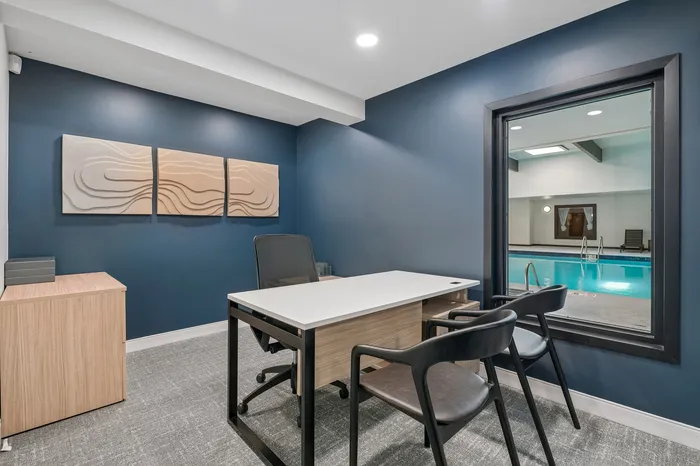 Elegant office space with modern desk and art decor, overlooking an indoor pool through a large window.