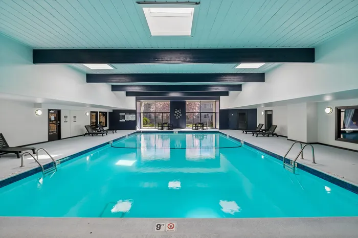 Luxurious indoor pool area featuring modern lounge chairs, bright skylights, and expansive windows offering a serene view.