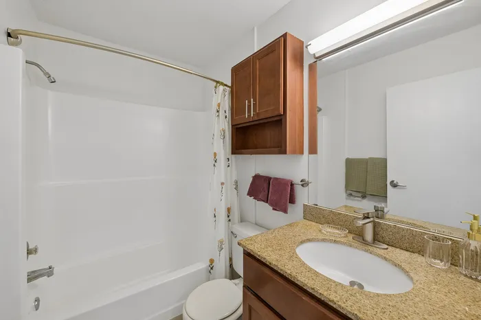 Modern bathroom featuring elegant granite countertop, stylish wood cabinetry, and pristine white bathtub with floral curtain.