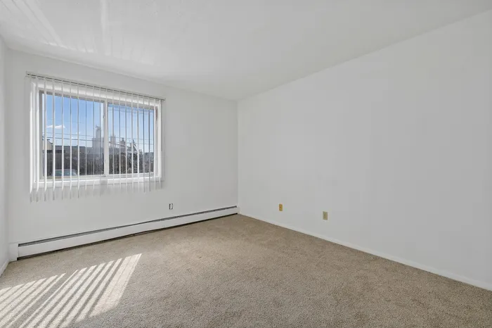 Bright and airy room with large window, soft carpeting, and clean white walls, perfect for customizing your personal space.