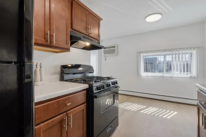 Bright, modern kitchen with rich wooden cabinetry, sleek black appliances, and a sunlit window enhancing the spacious feel.