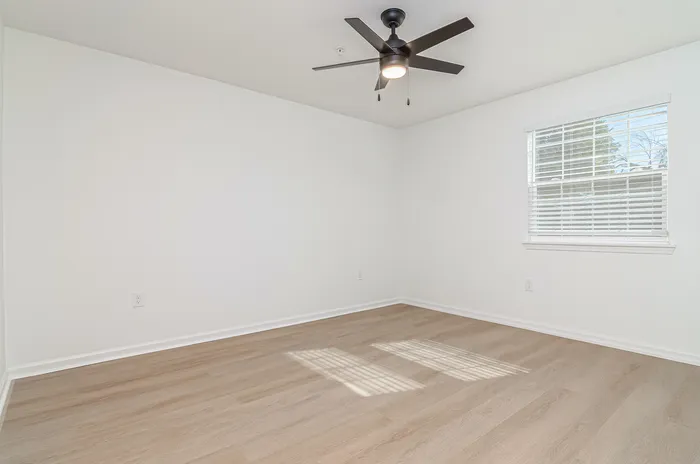 Bright, spacious room with sleek wood flooring and modern ceiling fan, offering ample natural light through a large window.