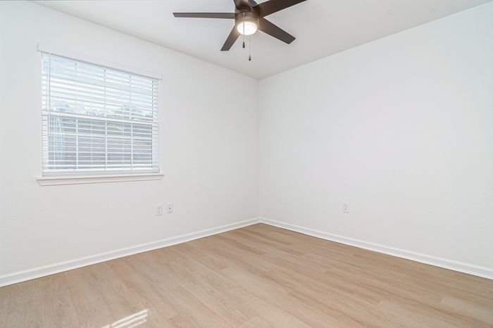 Bright and airy room featuring sleek hardwood floors, a ceiling fan, and a large window for natural light.