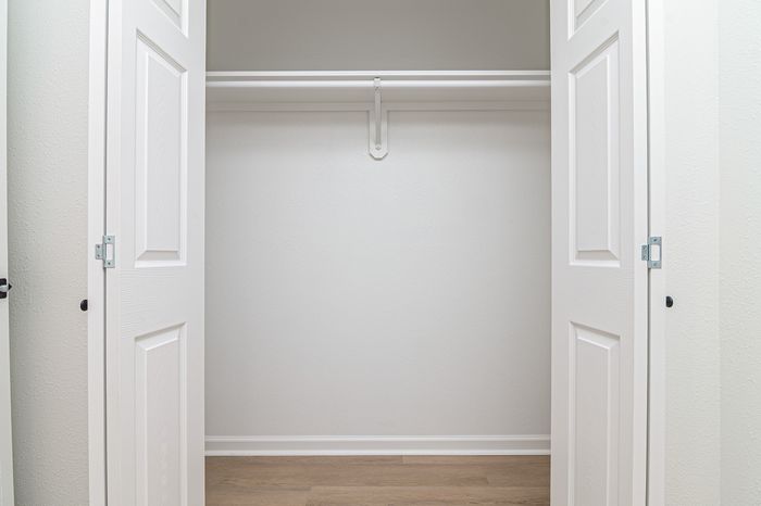 Spacious walk-in closet with sleek white double doors and wooden flooring, perfect for organized living.