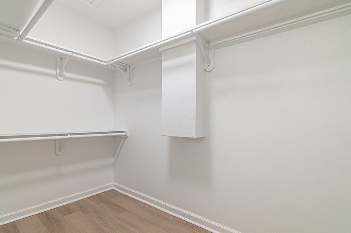 Spacious walk-in closet with light wood flooring, sleek white walls, and ample shelving for organized storage.