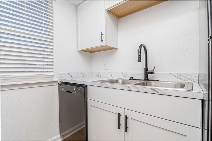 Chic modern kitchen with sleek white cabinets, marble countertops, dual sink, and stainless steel dishwasher.